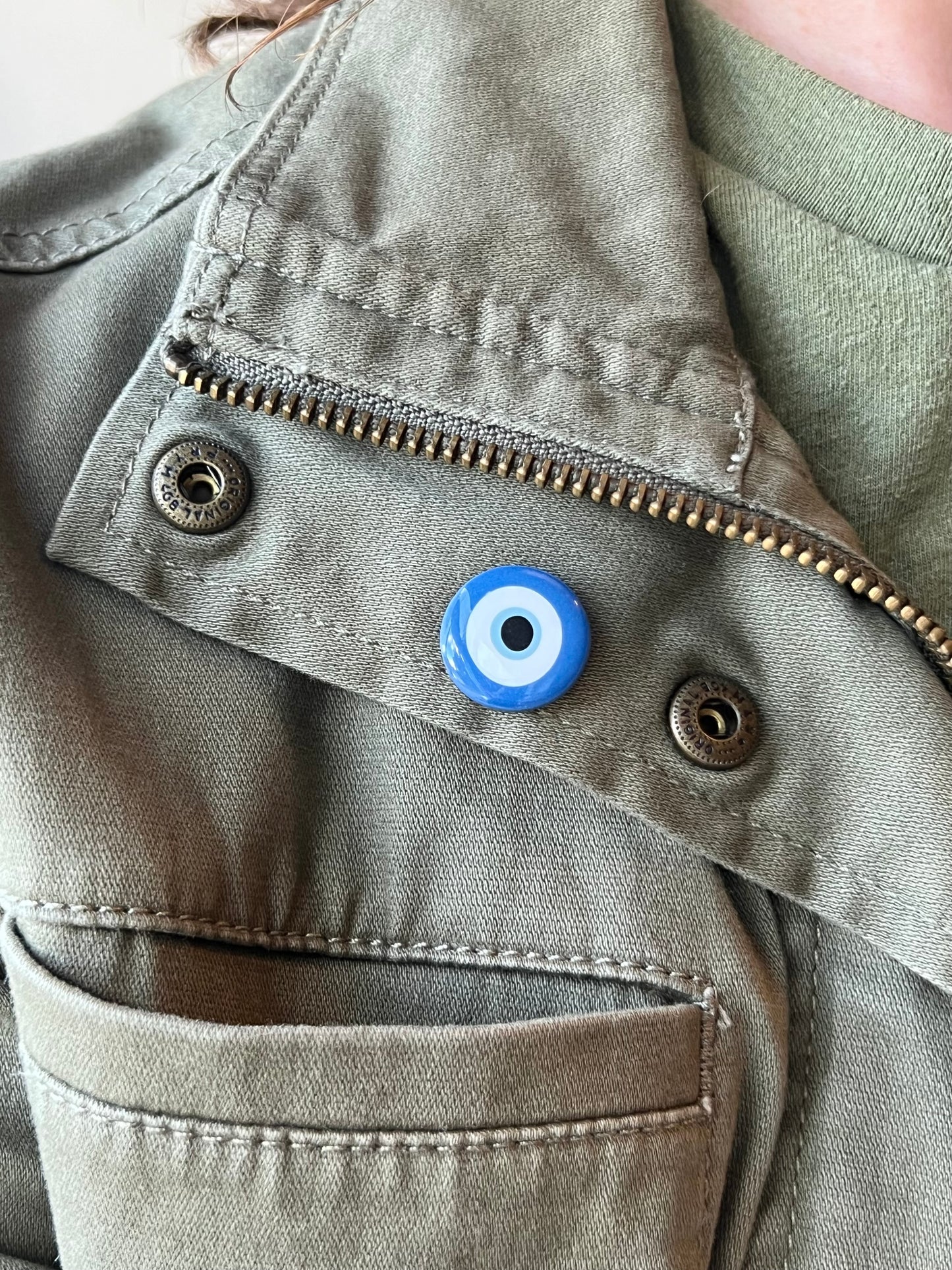Close-up of a green jacket with a blue evil eye charm on a beige background