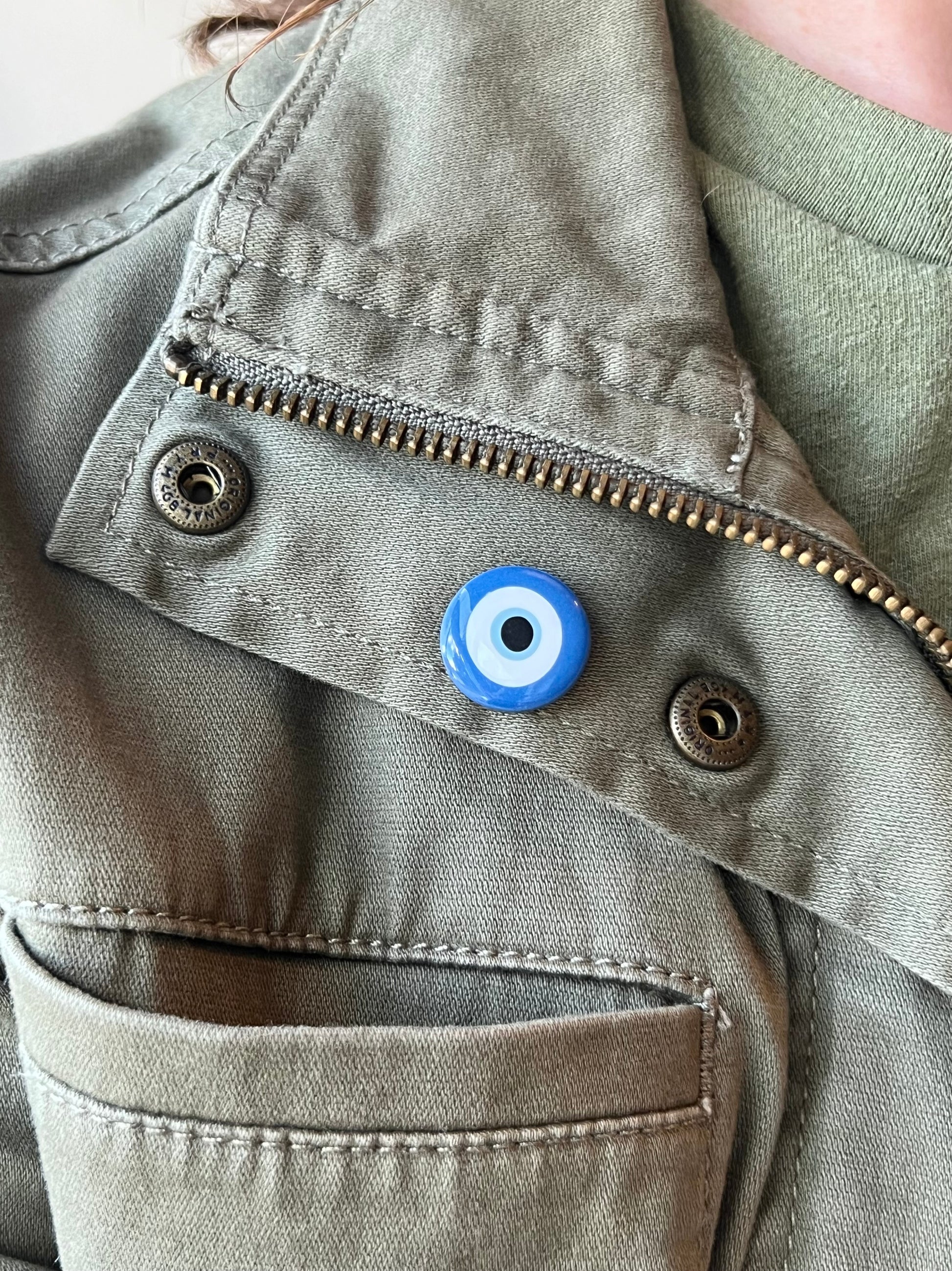 Close-up of a green jacket with a blue evil eye charm on a beige background