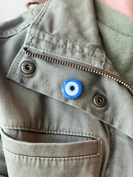Close-up of a green jacket with a blue evil eye charm on a beige background