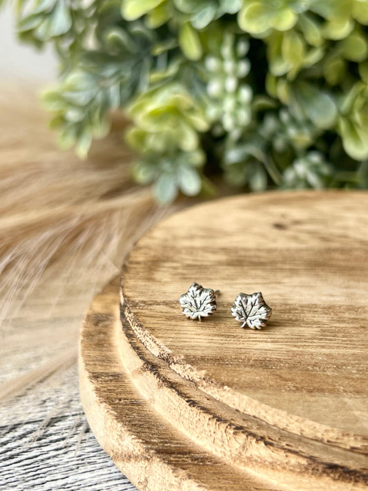 two silver maple leaf stud earrings on a wood surface
