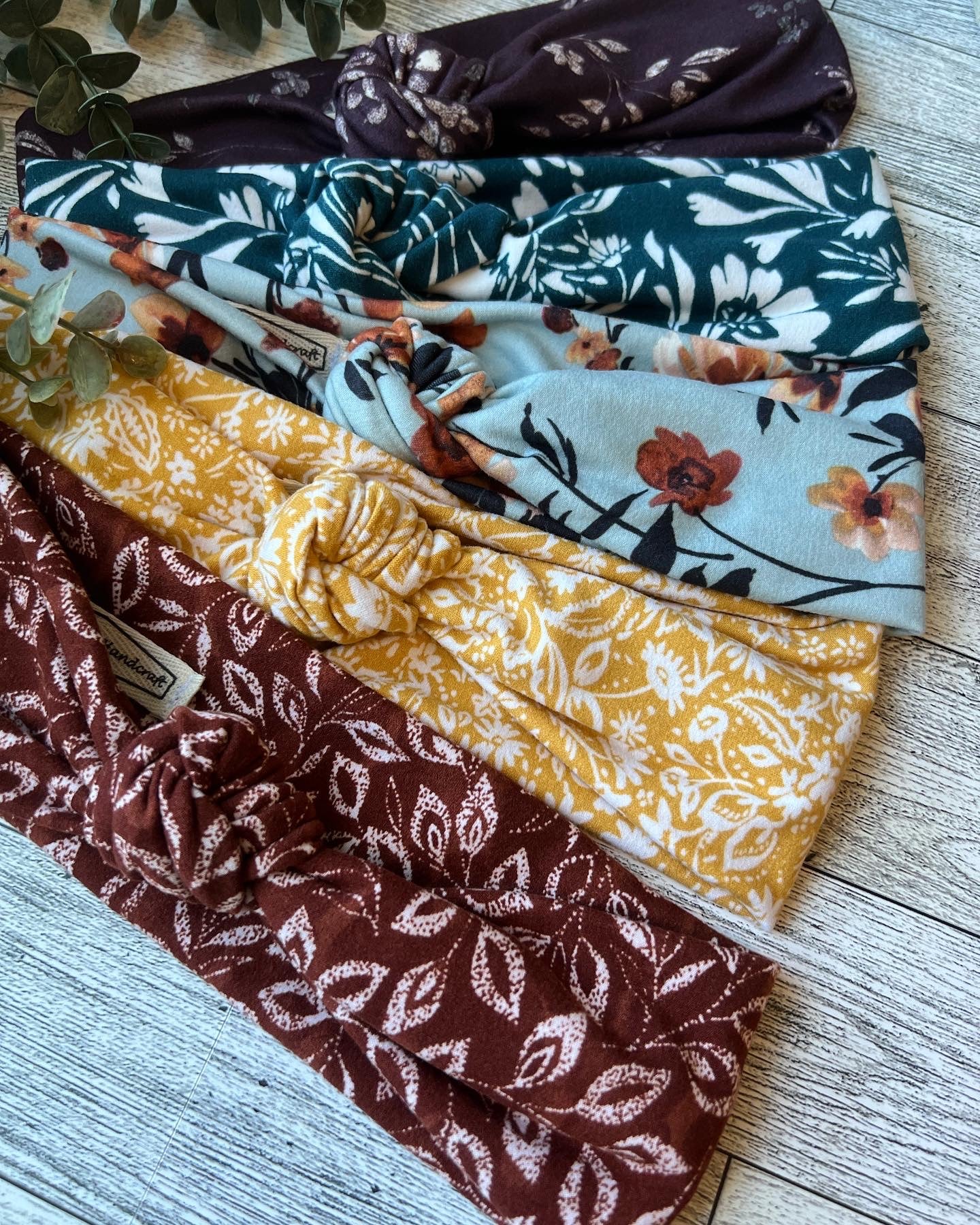 five knotted headbands in flower prints laid on a gray wood surface