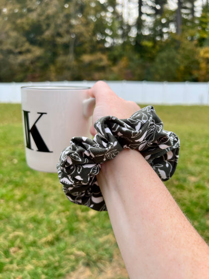 olive green hair scrunchie with white leaf pattern is worn on a wrist
