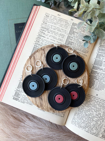 three pairs of vinyl record earrings with green, blue, and red labels on a wood surface